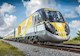 A black and gray bullet train with yellow and white designs on the front and side goes down a set of train tracks. The word, “brightline” in lowercase letters appears on the front and side of the train. 