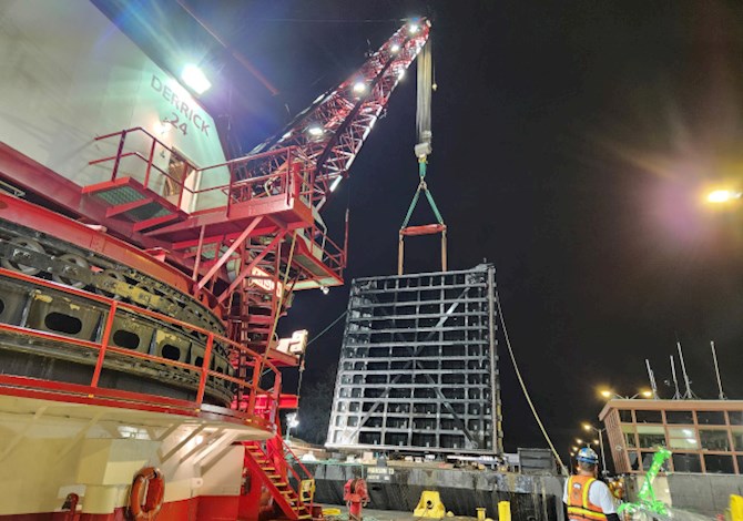 Nighttime construction view of the Lake Washington Ship Canal large lock miter gate replacement, with cranes lifting a massive steel gate.