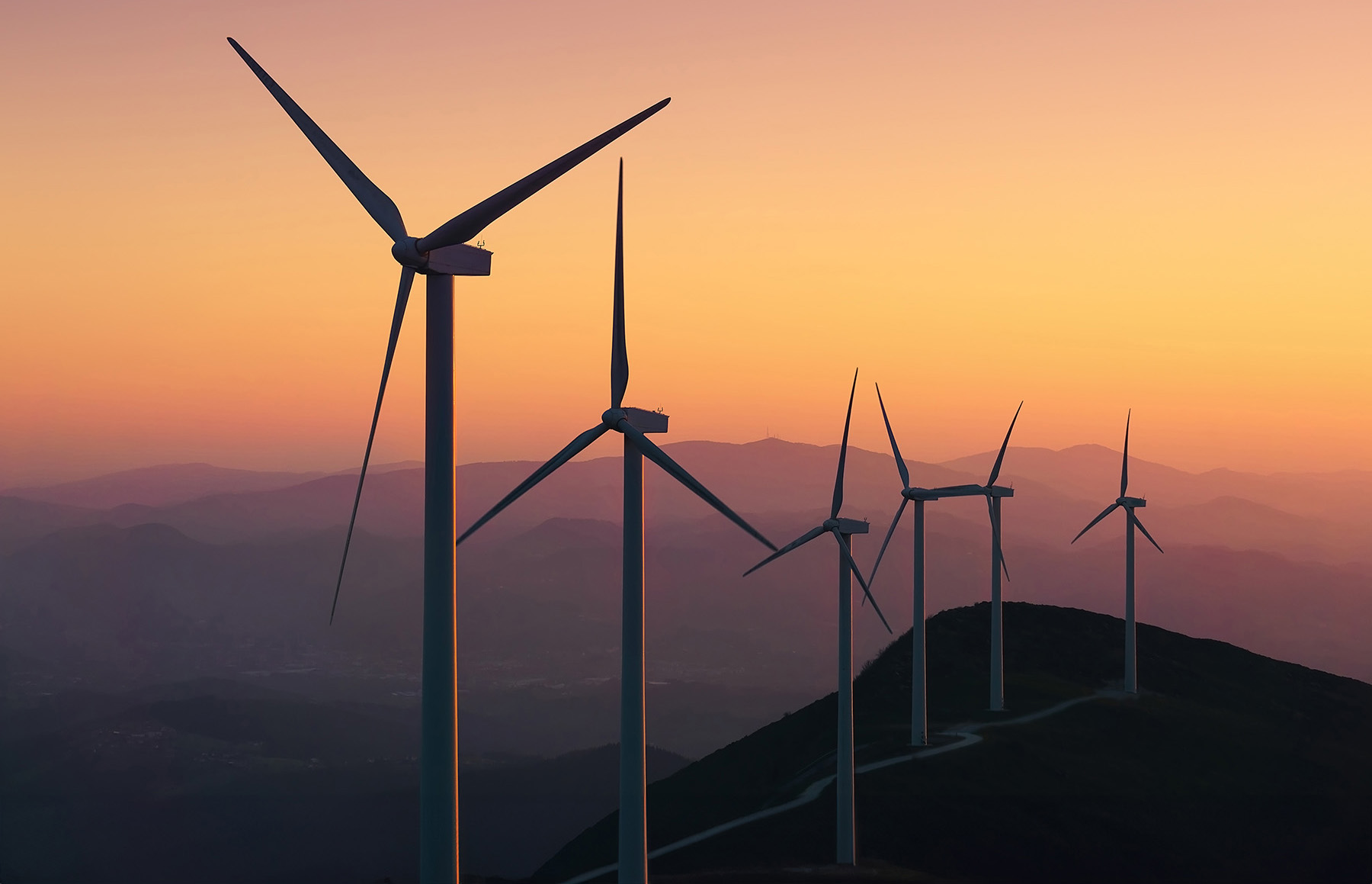 Six 3-blade while windmills are lined up on a mountainous parcel of land. 