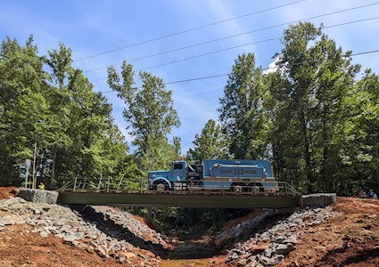 A blue commercial truck crosses a steel bridge. Below the bridge is water. 