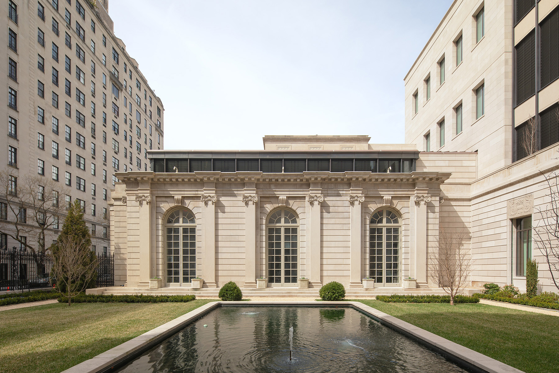 Image shows several multistory stone buildings. The building in the center has a rectangular pool in front of it. 