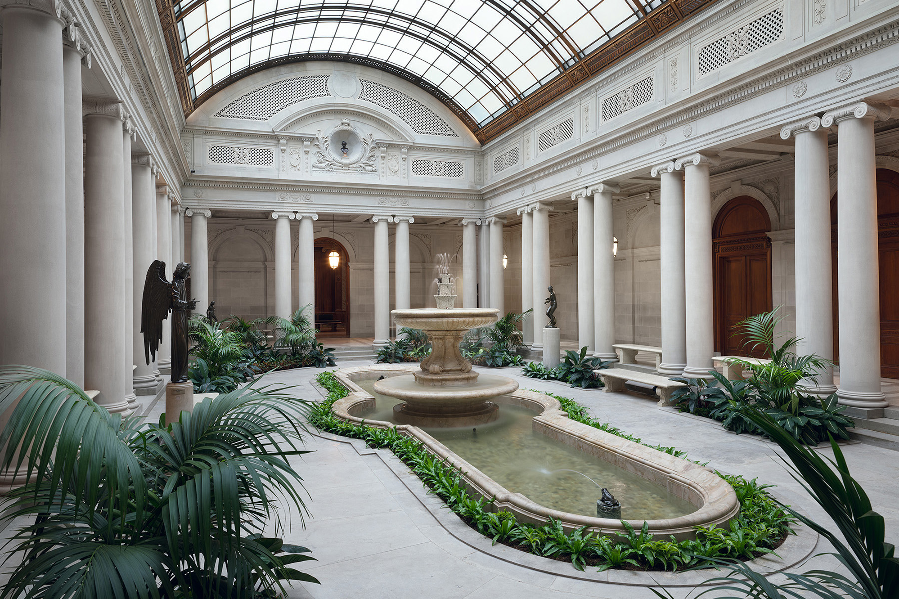 An inner courtyard has a oblong-shaped pool with a fountain in it. 
