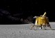 A rendering of a four-legged square-ish gold, shimmering piece of equipment stands upright on the surface of the moon. 
