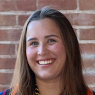 A woman with brown hair wearing a colorful top smiles at the camera. 