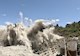 debris flies during a controlled blasting of a portion of a dam
