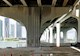 image showing underside of a bridge with constructions cones in the foreground and a water body and skyscrapers in the background