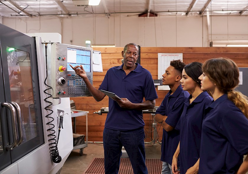 An educator teaching engineering students in front of machinery.
