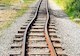 Railroad track with pronounced curve running through gravel and grassy surroundings